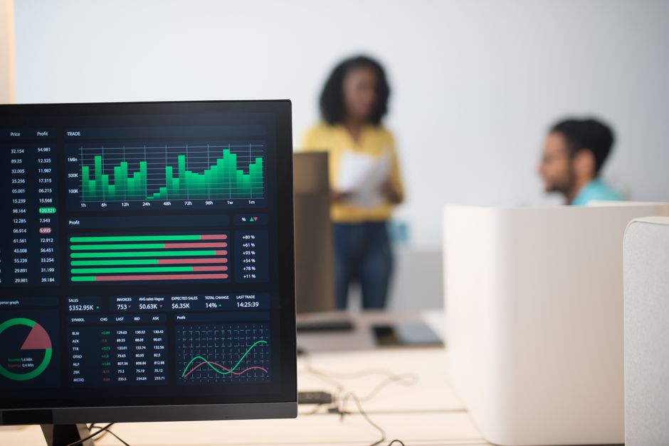 Tableau de bord de monitoring multi-panneaux sur écran avec graphiques en temps réel et équipe professionnelle en arrière-plan