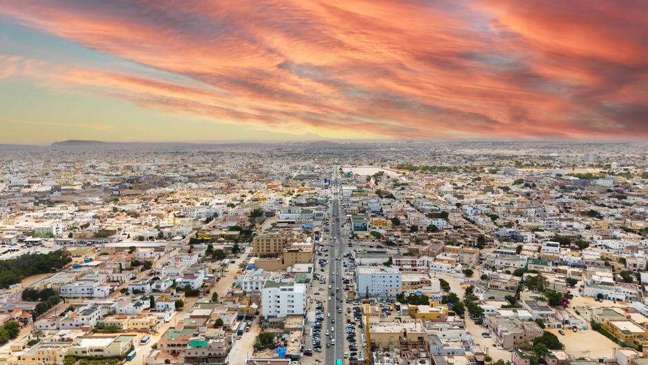 Vue aérienne de Nouakchott au coucher du soleil, avec un vaste boulevard et l'étalement urbain de la capitale mauritanienne
