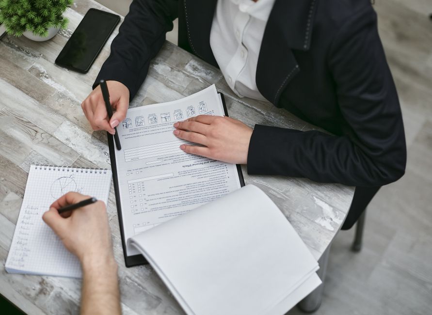 Deux professionnels en costume examinent des formulaires administratifs sur un bureau lors d'une réunion de travail